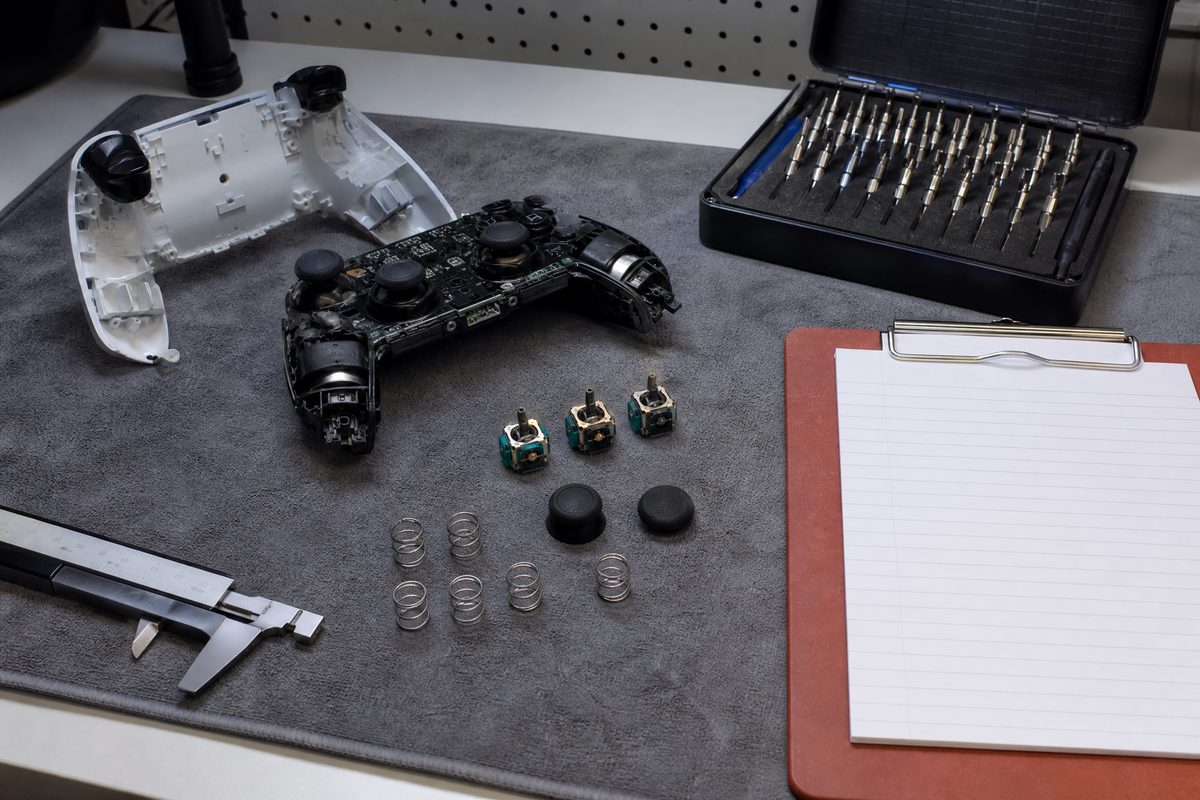 A controller partly disassembled on a workbench beside precision screwdrivers and a notebook covered in input timings